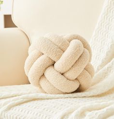 a white blanket on top of a couch next to a pillow with a knot in the middle