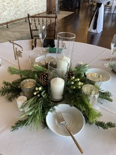 the table is set with pine cones, candles and evergreen greenery for an elegant centerpiece