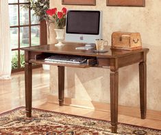 a desk with a computer on it in front of two pictures and a vase filled with flowers