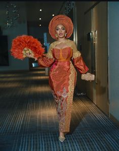 a woman in a red and gold dress is walking down the hallway with an orange fan