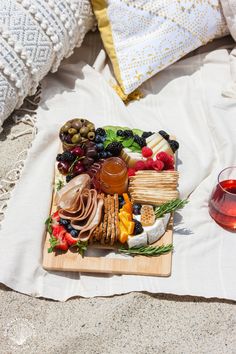 a platter of cheese, crackers and fruit on a blanket with a glass of wine