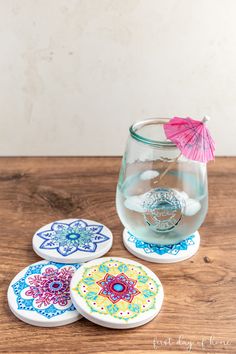 three coasters with designs on them and an umbrella in the middle, sitting on a wooden table