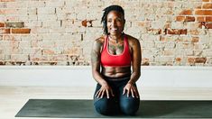 a woman sitting on a yoga mat in front of a brick wall with her arms crossed