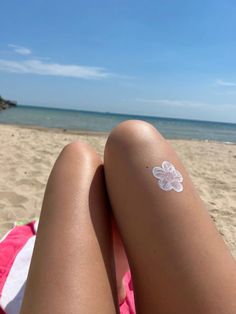 a person laying on top of a beach next to the ocean with a white flower tattooed on their arm