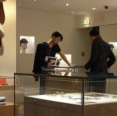 two people looking at jewelry in a display case with other items on the shelves behind them