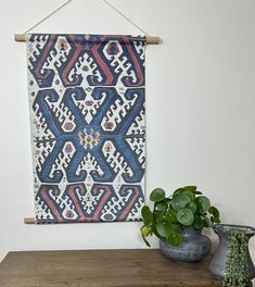 a blue and red wall hanging next to a potted plant on top of a wooden table