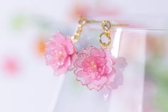 a pair of pink flower earrings sitting on top of a white vase filled with water