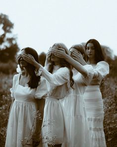 three women in white dresses are covering their eyes