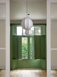 an empty room with green doors and two white lamps hanging from the ceiling above them