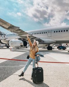 a woman standing in front of an airplane with her hand up and luggage on the ground