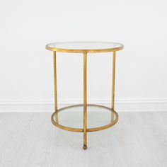 a round glass table with gold metal frame and wood legs on a white wooden floor