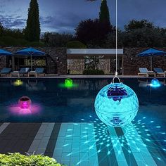 an illuminated pool ball floating in the middle of a swimming pool with lounge chairs and umbrellas around it