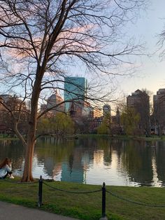 a woman sitting on a bench next to a body of water in a city park