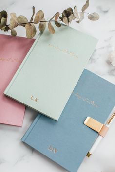 three notebooks sitting next to each other on top of a white table with flowers