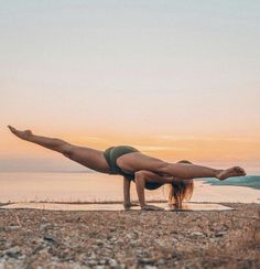 a woman doing a handstand in front of the ocean with her legs spread out