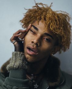 a young man with curly hair is talking on the phone and holding his hand to his ear