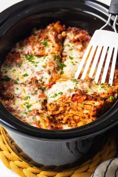 a close up of a fork in a slow cooker filled with lasagna