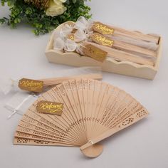 two wooden fans with tags on them sitting next to a bouquet of flowers in a box