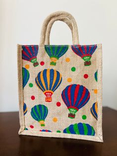 a jute bag with colorful hot air balloons printed on the front and sides, sitting on a wooden table