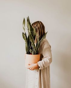 a woman holding a potted plant in front of her face and back to the camera