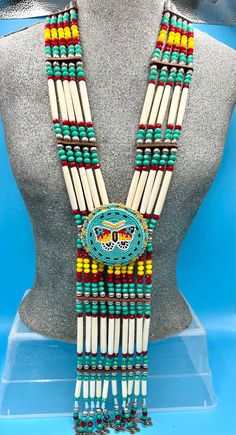 Bone hairpipes and crystal beads are often seen as part of traditional Native American dancers.  This modified breastplate  has been created to proudly proclaim that this is a good day to be Indigenous . It is designed to be worn not only in the dance circle, but in mainstream life, showing your Native pride and fashion sense.   The necklace is 10 vertical strands of bone hairpipes, nickel beads and 8mm sparking, faceted, fire-polished glass crystal green- turquoise , cranberry, tangerine and yellow sun beads The centerpiece is a beaded rosette of a fanciful colorful butterfly,  on a background of green-turquoise beads.   At the bottom of breastplate, fully detailed, three dimensional butterflies add their music to your movements. The breastplate comes with matching earrings on stainless s Bone Jewellery, Indigenous Jewelry, Bone Bead Necklace, Breast Plate, Native American Jewellery, Loom Designs, Turquoise Butterfly, Native Wears, Stone Bead Jewelry