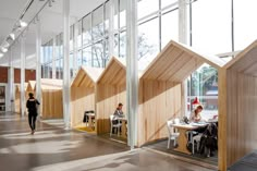 people are sitting at tables in an open area with large windows and wooden structures on the walls