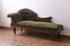 a green couch sitting on top of a wooden floor next to a white walled wall