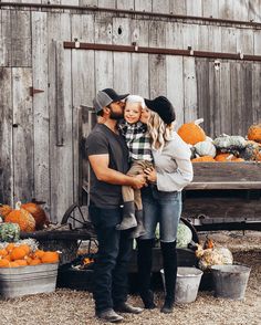 a man and woman standing next to each other in front of a wooden fence with pumpkins