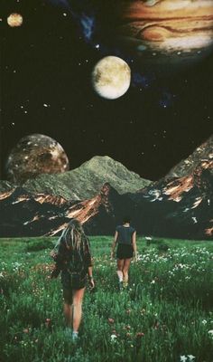 two people are walking through the grass with mountains in the background, and one person is looking up at the sky