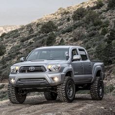 a gray toyota truck parked on top of a dirt road in front of a mountain