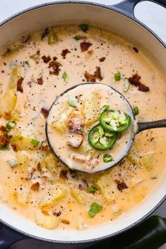 a ladle full of soup with potatoes, bacon and jalapenos in it