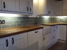 a kitchen with white cabinets and wood counter tops in front of a gray tile backsplash