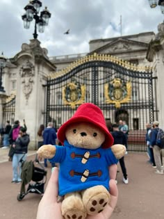 a person holding a small teddy bear in front of a building with ornate iron gates