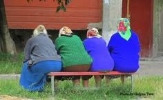 three women sitting on a bench with their backs to each other, wearing colorful sweaters