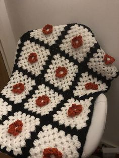 a black and white crocheted blanket with red flowers on it sitting on a chair