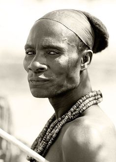 a black and white photo of a man with no shirt on, holding a stick