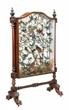 a wooden frame with birds on it and an ornate stand holding a glass display case