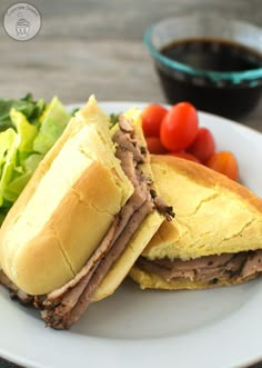 a white plate topped with a cut in half sandwich next to lettuce and tomatoes