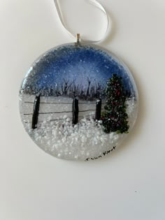 a glass ornament with a christmas tree and fence in the snow on a white background