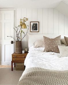 a bed with white sheets and pillows in a bedroom next to a wooden dresser topped with vases