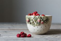 a white bowl filled with raspberries sitting on top of a wooden table next to some leaves