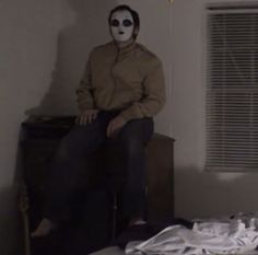 a man sitting on top of a bed in a room with a white painted face