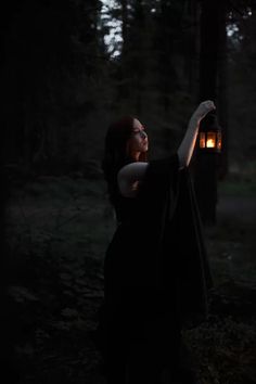 a woman holding up a lantern in the dark forest at night with her eyes closed