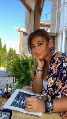 a woman is sitting at a table with her hand on her chin and looking into the camera