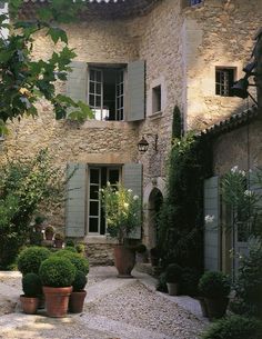 a stone house with green shutters and potted plants