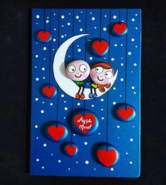 a card with two people on the moon and hearts hanging from it's sides