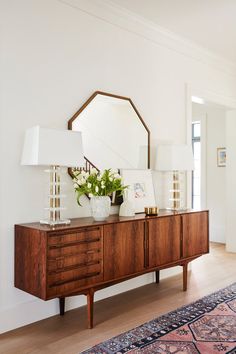 a room with a dresser, mirror and lamp on it's sideboard next to a rug