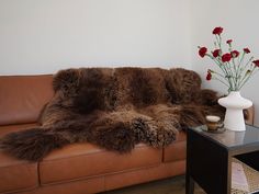 a brown leather couch sitting next to a vase with flowers in it on top of a table