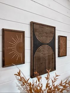 three framed art pieces hanging on the side of a white wall next to a potted plant