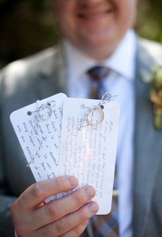 a man in a gray suit holding two wedding tags with rings on them and flowers